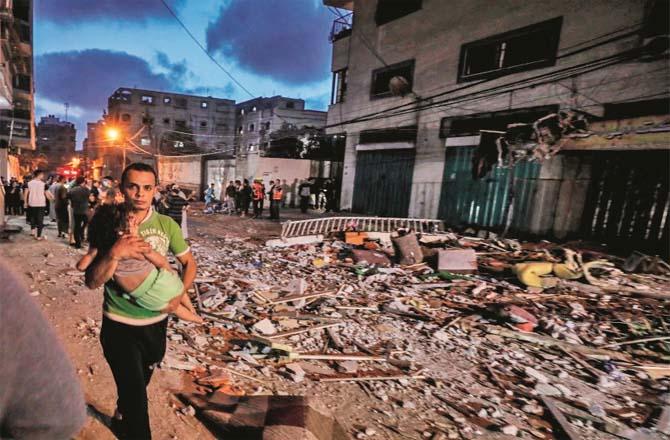 A man carries a small child to safety in the aftermath of an Israeli attack.Picture:PTI